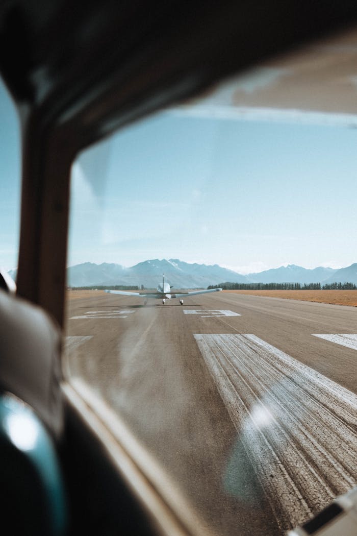 View from an airplane window of a runway in Wanaka, New Zealand, surrounded by mountains.