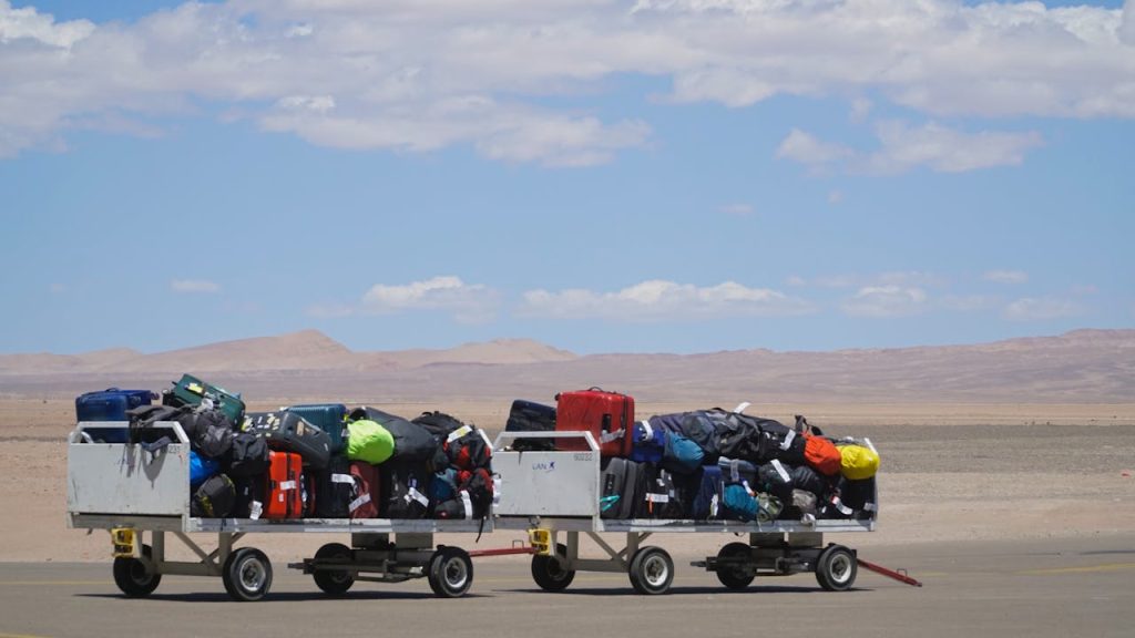 Luggage carts at airport loaded with colorful bags under clear sky. Outdoor travel scene.