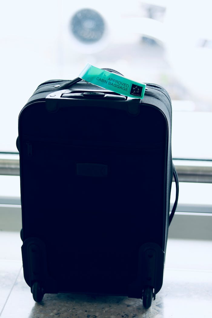 Close-up of a black suitcase with a cabin approved tag in airport setting.