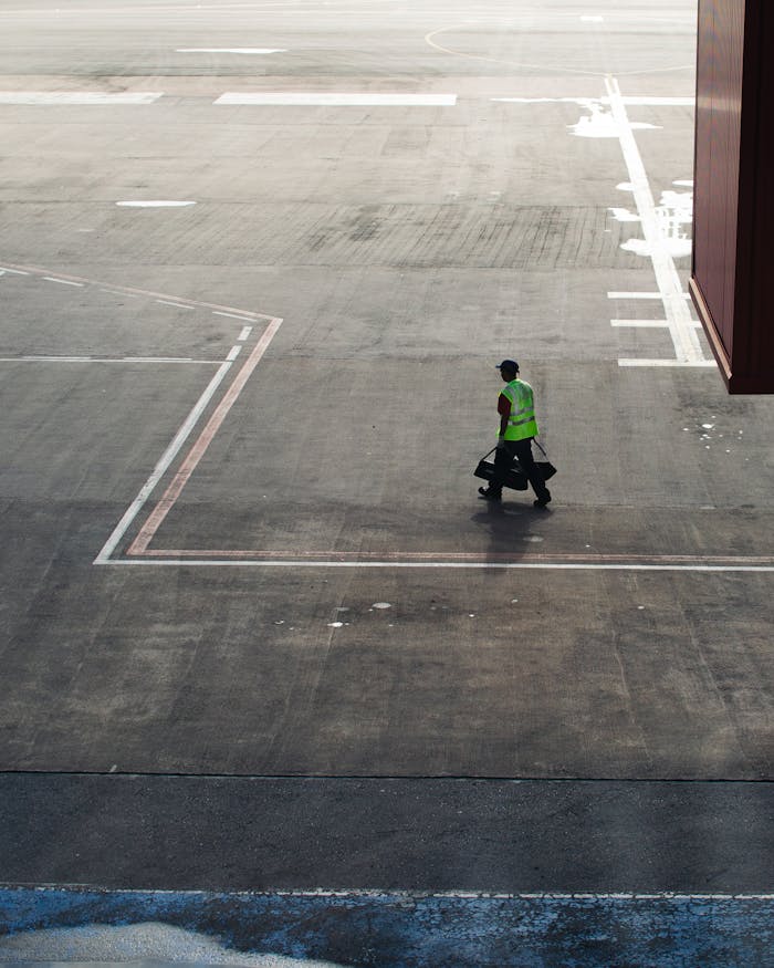 Airport worker in high-visibility gear walking on a sunny airport tarmac in Brazil.